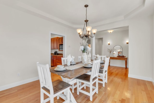 dining space with an inviting chandelier, a tray ceiling, and light hardwood / wood-style floors