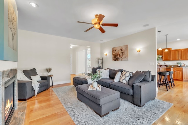 living room with ceiling fan, a high end fireplace, and light hardwood / wood-style floors