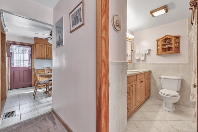 bathroom featuring ceiling fan, tile patterned flooring, tile walls, vanity, and toilet