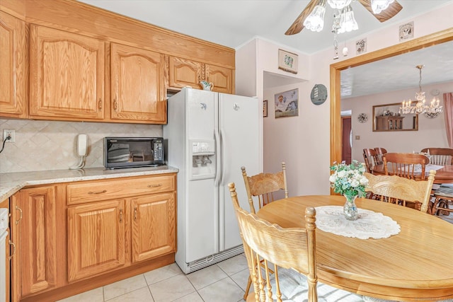 kitchen with light tile patterned flooring, white refrigerator with ice dispenser, light stone countertops, ceiling fan with notable chandelier, and decorative backsplash