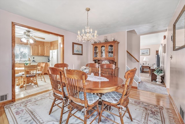 dining area with ceiling fan with notable chandelier and light hardwood / wood-style flooring