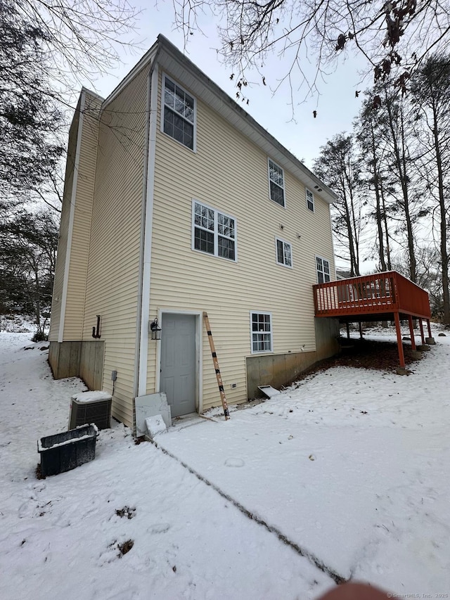 snow covered rear of property featuring central air condition unit, a wooden deck, and a garage