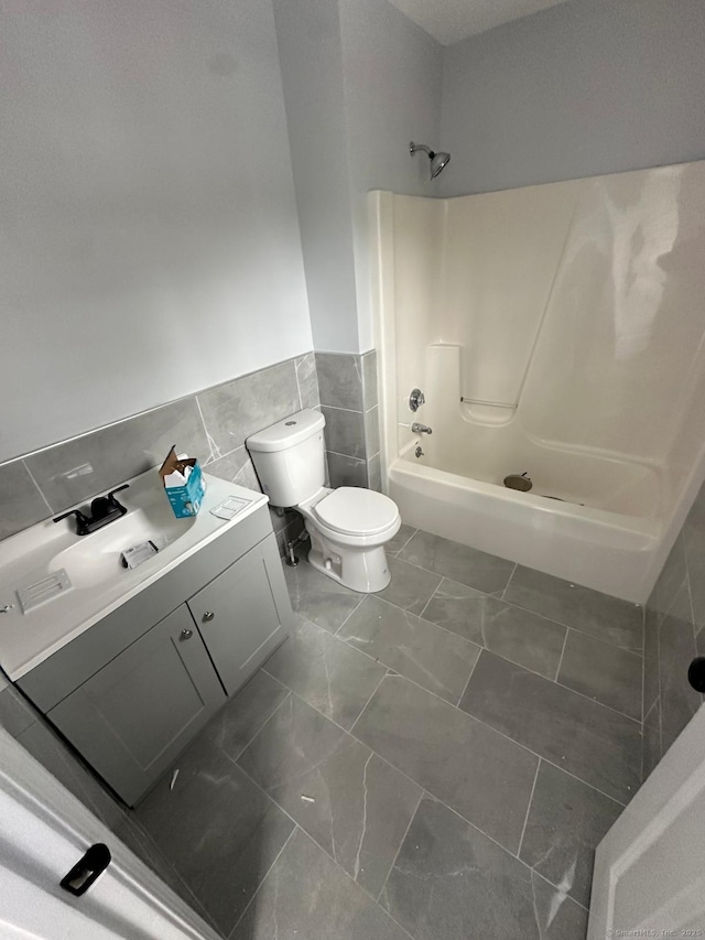 full bathroom with washtub / shower combination, toilet, vanity, and tile walls