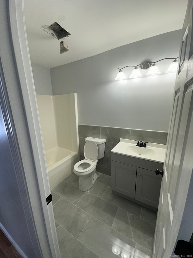 bathroom featuring toilet, vanity, tile patterned floors, and tile walls