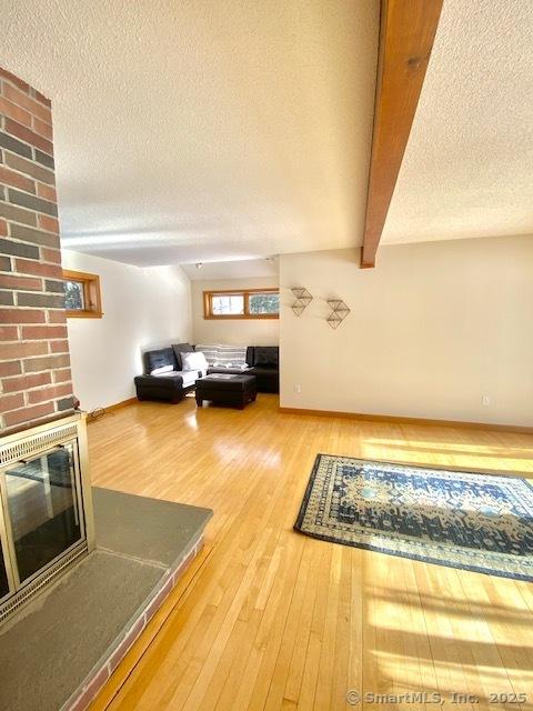 unfurnished living room featuring a brick fireplace, a textured ceiling, hardwood / wood-style flooring, and beam ceiling