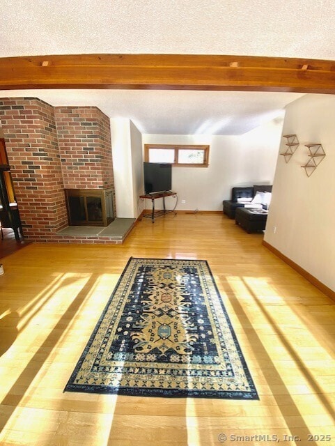 unfurnished living room with hardwood / wood-style flooring, a brick fireplace, and beam ceiling