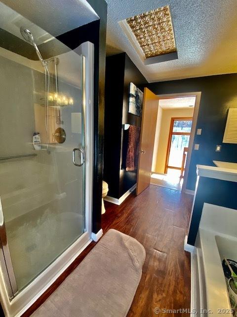 bathroom featuring hardwood / wood-style floors, toilet, a shower with door, and a textured ceiling