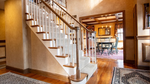 staircase with beamed ceiling, coffered ceiling, hardwood / wood-style floors, and a notable chandelier