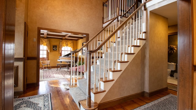 stairs featuring beamed ceiling, coffered ceiling, and hardwood / wood-style floors