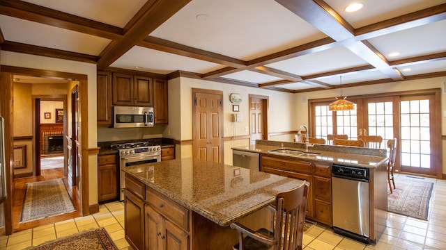 kitchen featuring sink, dark stone countertops, coffered ceiling, stainless steel appliances, and a center island with sink