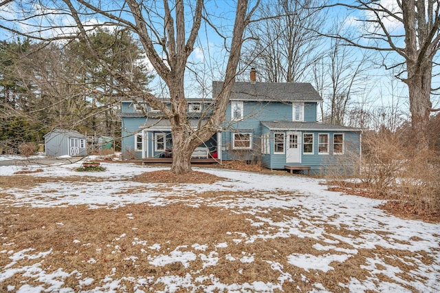 snow covered rear of property with a storage unit