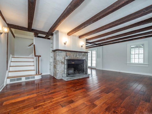 unfurnished living room featuring wood-type flooring, a stone fireplace, a healthy amount of sunlight, and beam ceiling