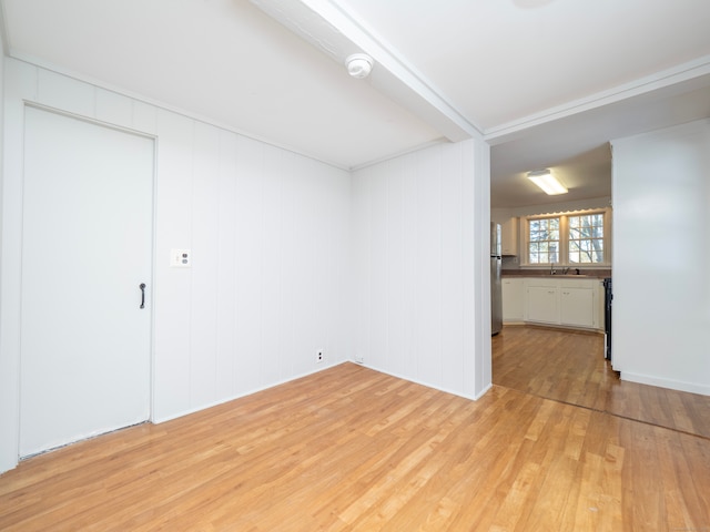 empty room featuring beam ceiling, sink, and light wood-type flooring