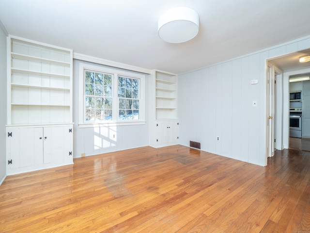 unfurnished living room featuring built in shelves and light hardwood / wood-style floors