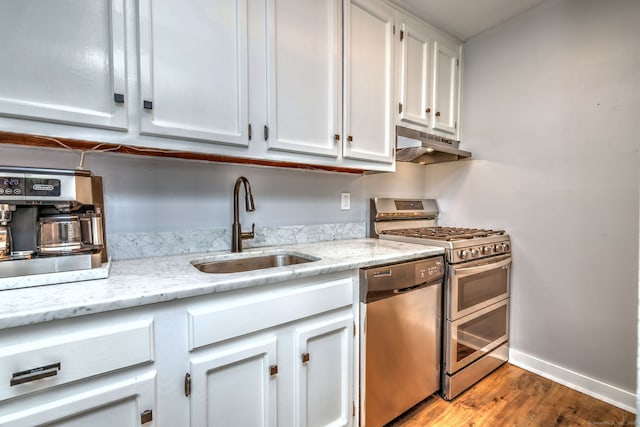 kitchen with appliances with stainless steel finishes, white cabinetry, sink, hardwood / wood-style flooring, and light stone counters