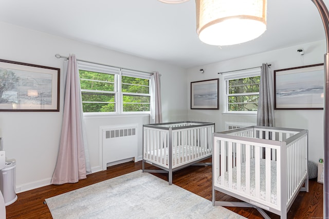 bedroom with multiple windows, radiator heating unit, dark hardwood / wood-style flooring, and a crib