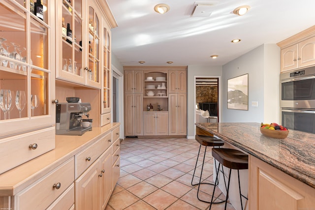 kitchen featuring light tile patterned floors, light brown cabinetry, stainless steel double oven, and a kitchen breakfast bar