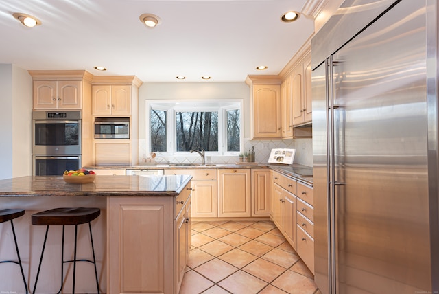 kitchen with a center island, dark stone counters, built in appliances, sink, and light tile patterned floors