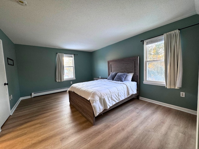 bedroom featuring multiple windows, a baseboard radiator, wood-type flooring, and a textured ceiling