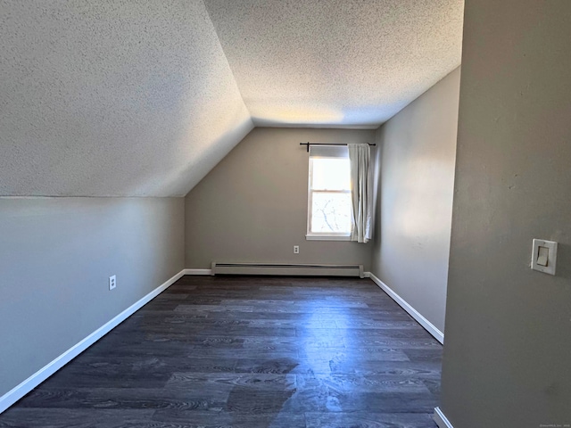 additional living space with dark wood-type flooring, vaulted ceiling, a textured ceiling, and baseboard heating