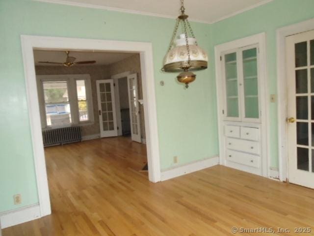 unfurnished dining area with ceiling fan, wood-type flooring, radiator heating unit, and crown molding