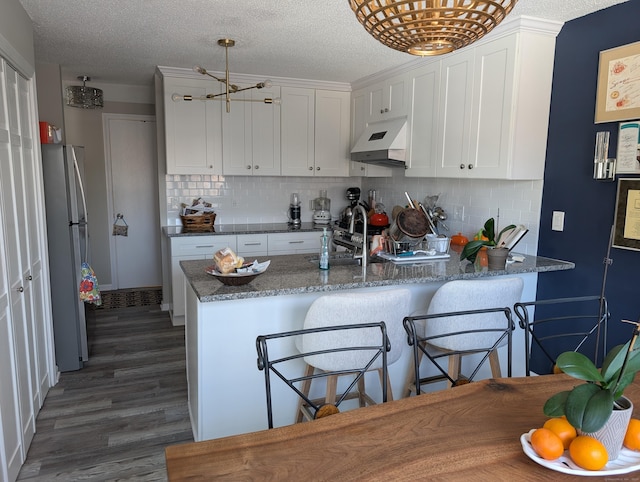 kitchen with sink, kitchen peninsula, stainless steel refrigerator, and white cabinets