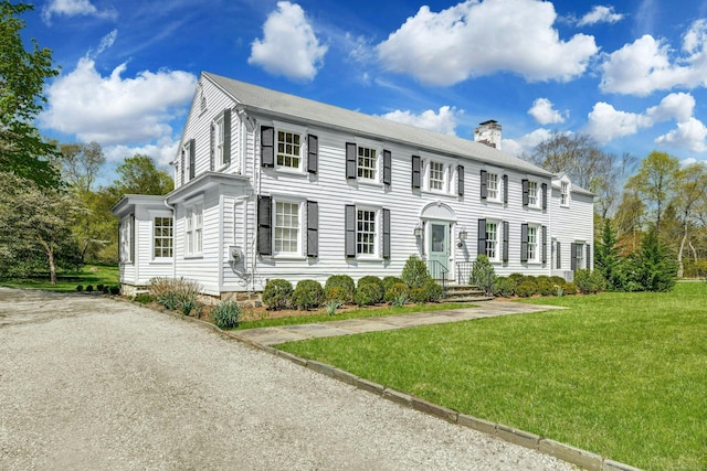 colonial inspired home featuring a chimney and a front lawn