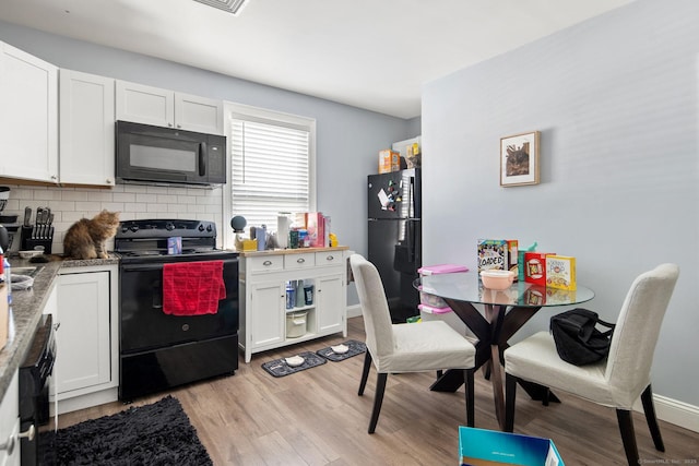 kitchen featuring white cabinetry, light wood-type flooring, black appliances, and tasteful backsplash