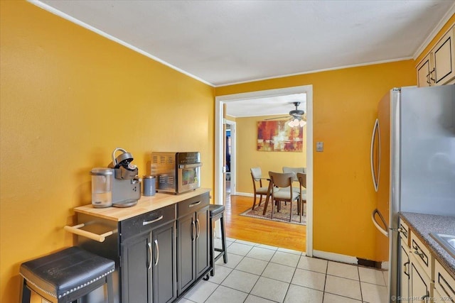 kitchen featuring stainless steel refrigerator, ceiling fan, ornamental molding, and light tile patterned floors