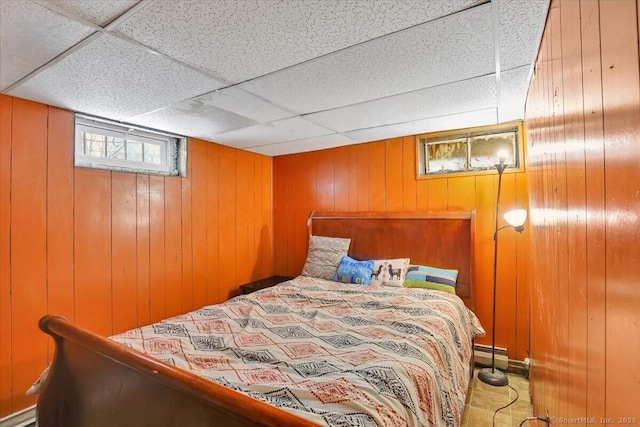 bedroom with a baseboard radiator, wooden walls, and a drop ceiling