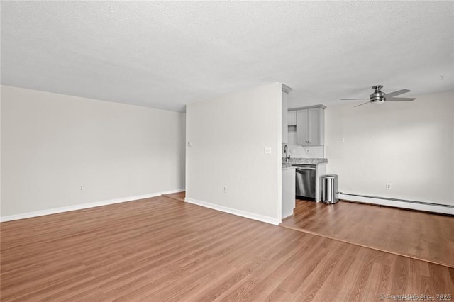 unfurnished living room featuring ceiling fan, a baseboard heating unit, a textured ceiling, and light wood-type flooring