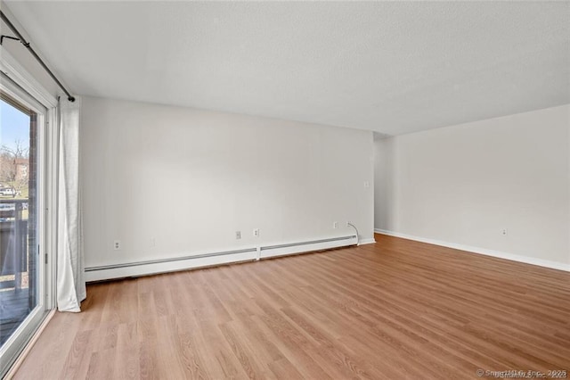 spare room featuring baseboard heating and light hardwood / wood-style floors