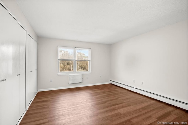 unfurnished bedroom featuring dark wood-type flooring and a baseboard heating unit