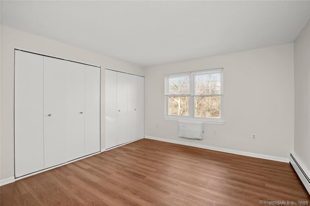 unfurnished bedroom featuring hardwood / wood-style flooring, two closets, and a baseboard heating unit