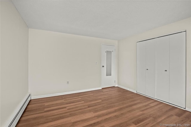 unfurnished bedroom with wood-type flooring, baseboard heating, and a closet