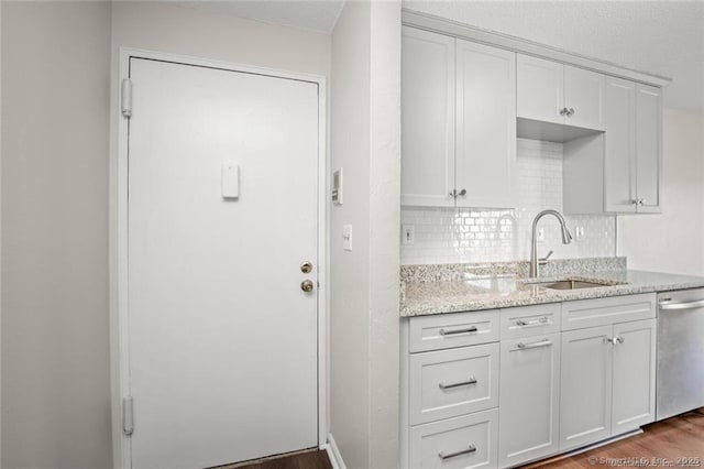 kitchen with sink, white cabinetry, dark hardwood / wood-style floors, light stone countertops, and stainless steel dishwasher