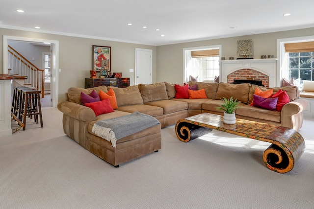 living room with a brick fireplace, light colored carpet, ornamental molding, and a healthy amount of sunlight