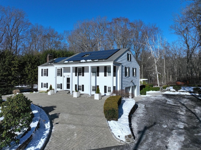 neoclassical home featuring driveway, a garage, entry steps, a chimney, and roof mounted solar panels