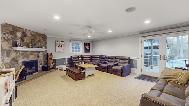 living room featuring french doors, a stone fireplace, ceiling fan, ornamental molding, and light colored carpet