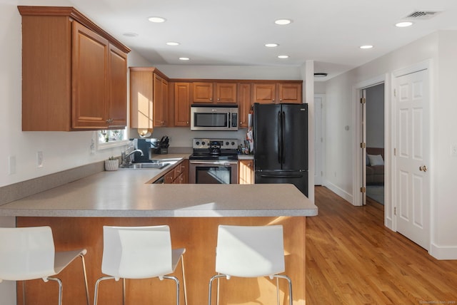 kitchen with kitchen peninsula, light hardwood / wood-style flooring, appliances with stainless steel finishes, sink, and a breakfast bar