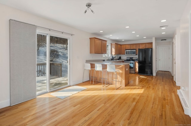 kitchen featuring baseboard heating, a kitchen bar, stainless steel appliances, light hardwood / wood-style floors, and kitchen peninsula