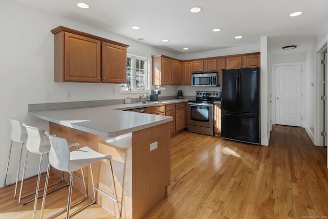 kitchen with kitchen peninsula, a kitchen breakfast bar, sink, light wood-type flooring, and stainless steel appliances