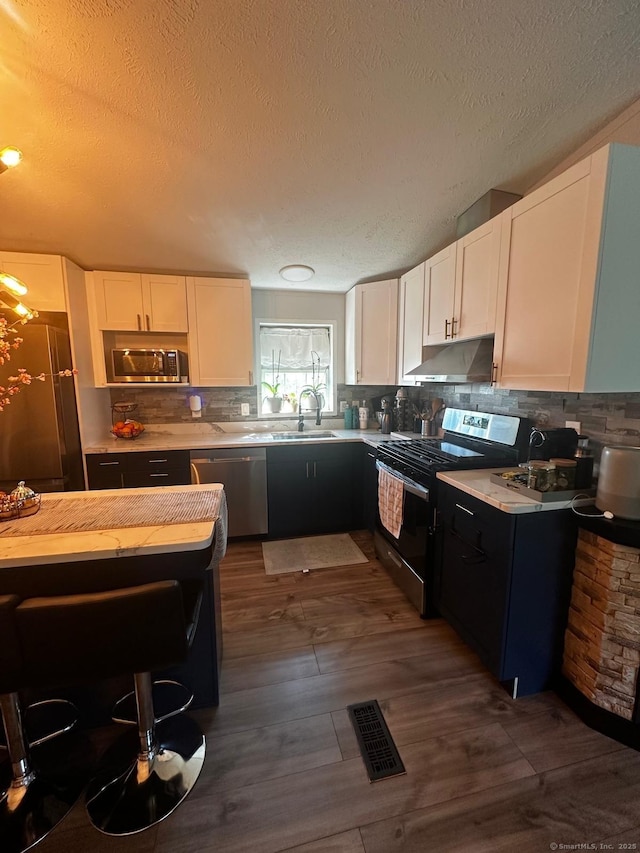 kitchen with decorative backsplash, stainless steel appliances, a textured ceiling, and white cabinets