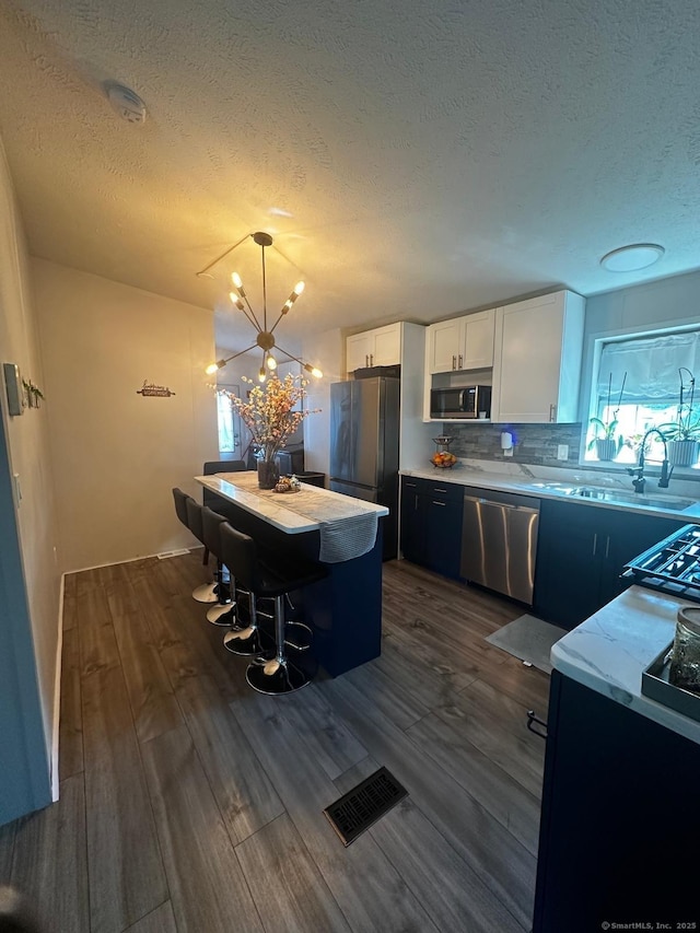 kitchen featuring appliances with stainless steel finishes, dark hardwood / wood-style floors, a kitchen island, pendant lighting, and white cabinets