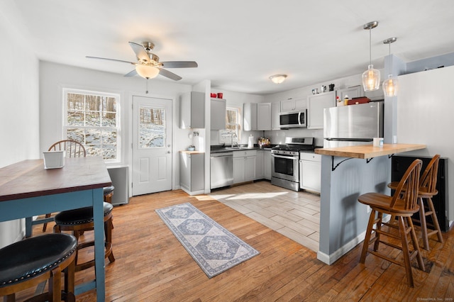 kitchen with kitchen peninsula, hanging light fixtures, sink, light wood-type flooring, and stainless steel appliances