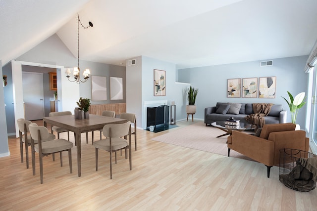 dining space featuring lofted ceiling, light wood finished floors, a fireplace with flush hearth, and visible vents