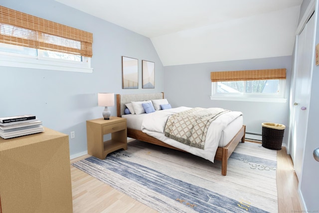 bedroom with lofted ceiling, light wood-type flooring, baseboards, and baseboard heating