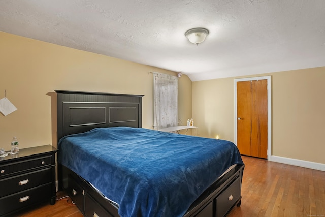 bedroom with hardwood / wood-style floors, a textured ceiling, and vaulted ceiling