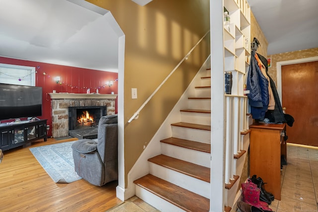 staircase with wood-type flooring and a stone fireplace