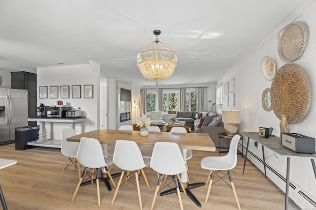 dining area featuring a notable chandelier, crown molding, a baseboard radiator, and light wood-type flooring